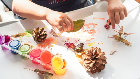 Preschooler pasting and painting leaving and pinecones on a piece of a paper