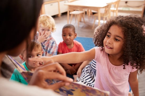 Image of preschooler pointing at something the teacher is reading